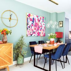 Duck egg blue open plan kitchen and dining room with orb pendant light, abstract artwork on wall, industrial dining table and blue velvet chairs
