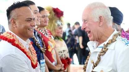 King Charles wearing a wood necklace and white shirt laughing as he talks to Samoan leaders