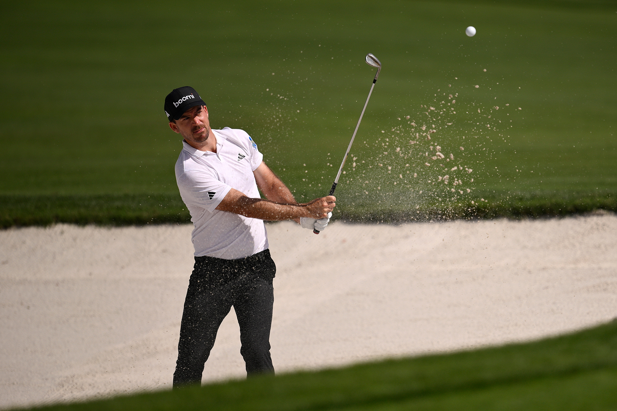 Nick Taylor hitting a bunker shot with sand flying up around the ball