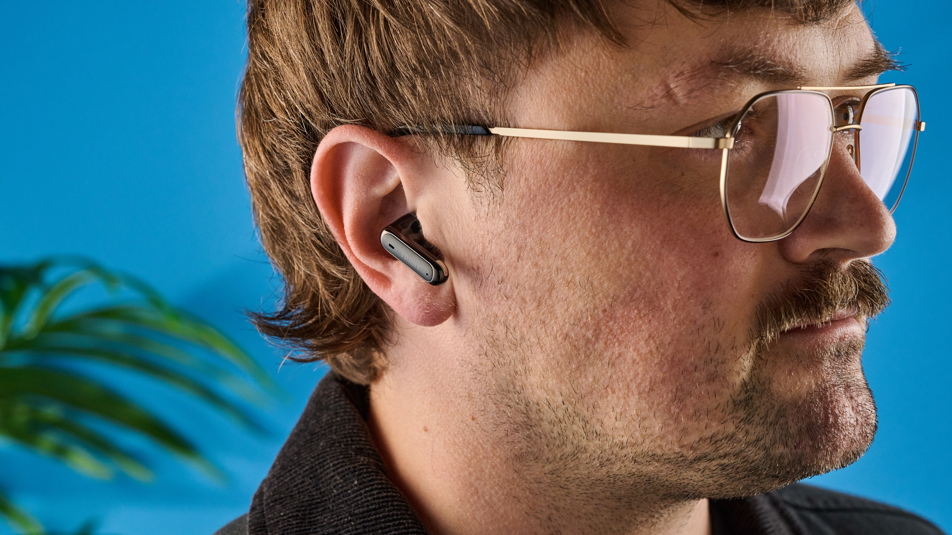 Tribit FlyBuds C3 in black photographed on a blue background with leaves
