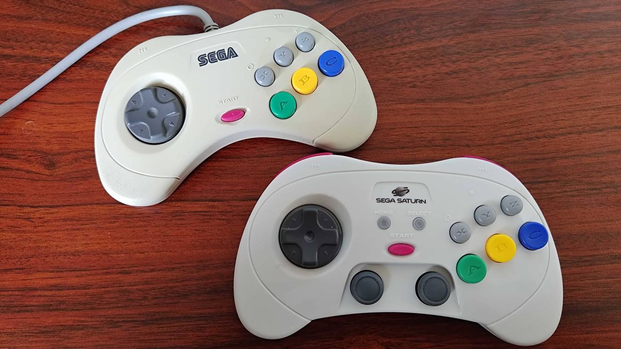 Retro-bit Sega Saturn controller next to original gamepad on woodgrain desk.