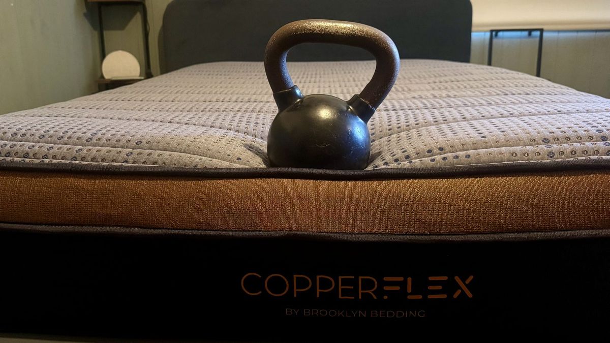 A black and metal kettle bell perched at foot of navy and bronze Brooklyn Bedding Copperflex Memory Foam mattress