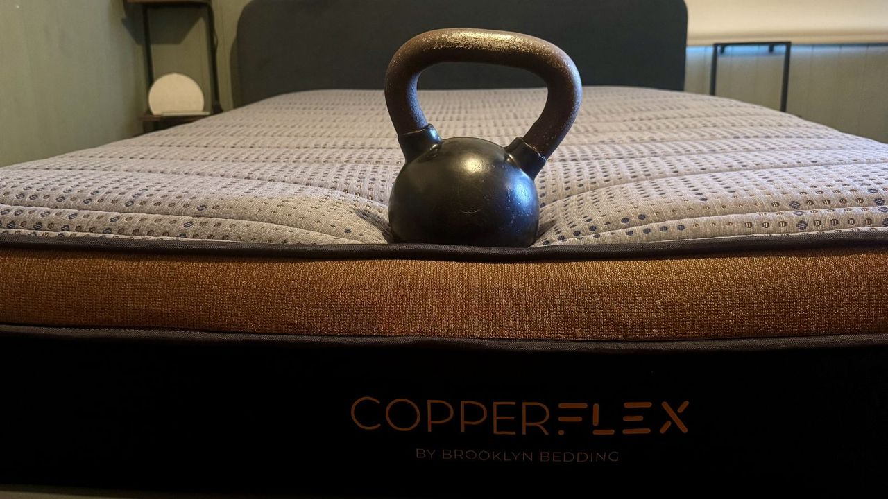 A black and metal kettle bell perched at foot of navy and bronze Brooklyn Bedding Copperflex Memory Foam mattress