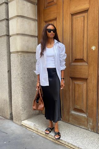 summer wardrobe essential shown on a woman wearing an oversized button-down shirt over a tank with a slip skirt and slide sandals