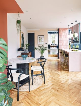 Kitchen-diner with pink walls, parquet floor, pink kitchen island, and black and marble table and chairs