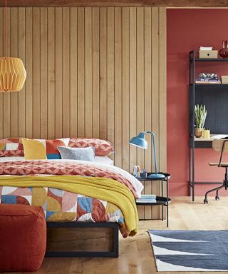Habitat red and yellow bedroom with wood paneling and blue bed side lamp