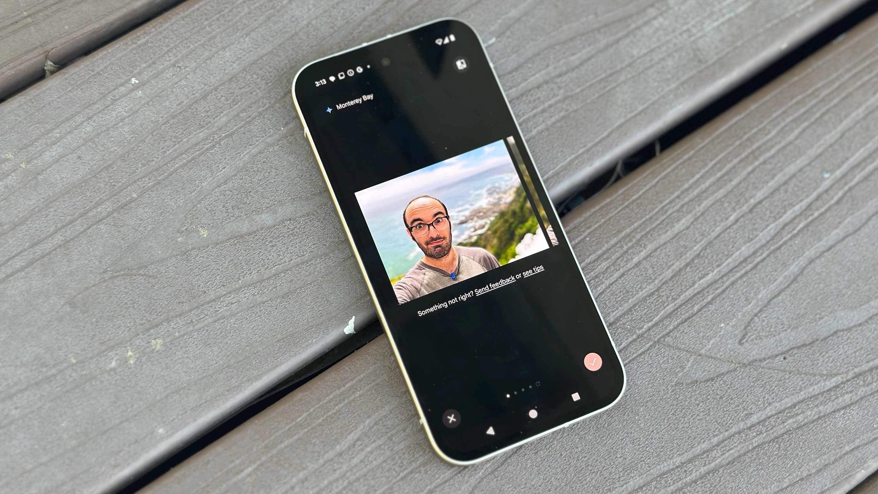 The Google Pixel 9a sitting on a deck, showing a selfie edited with Magic Editor to add an ocean.
