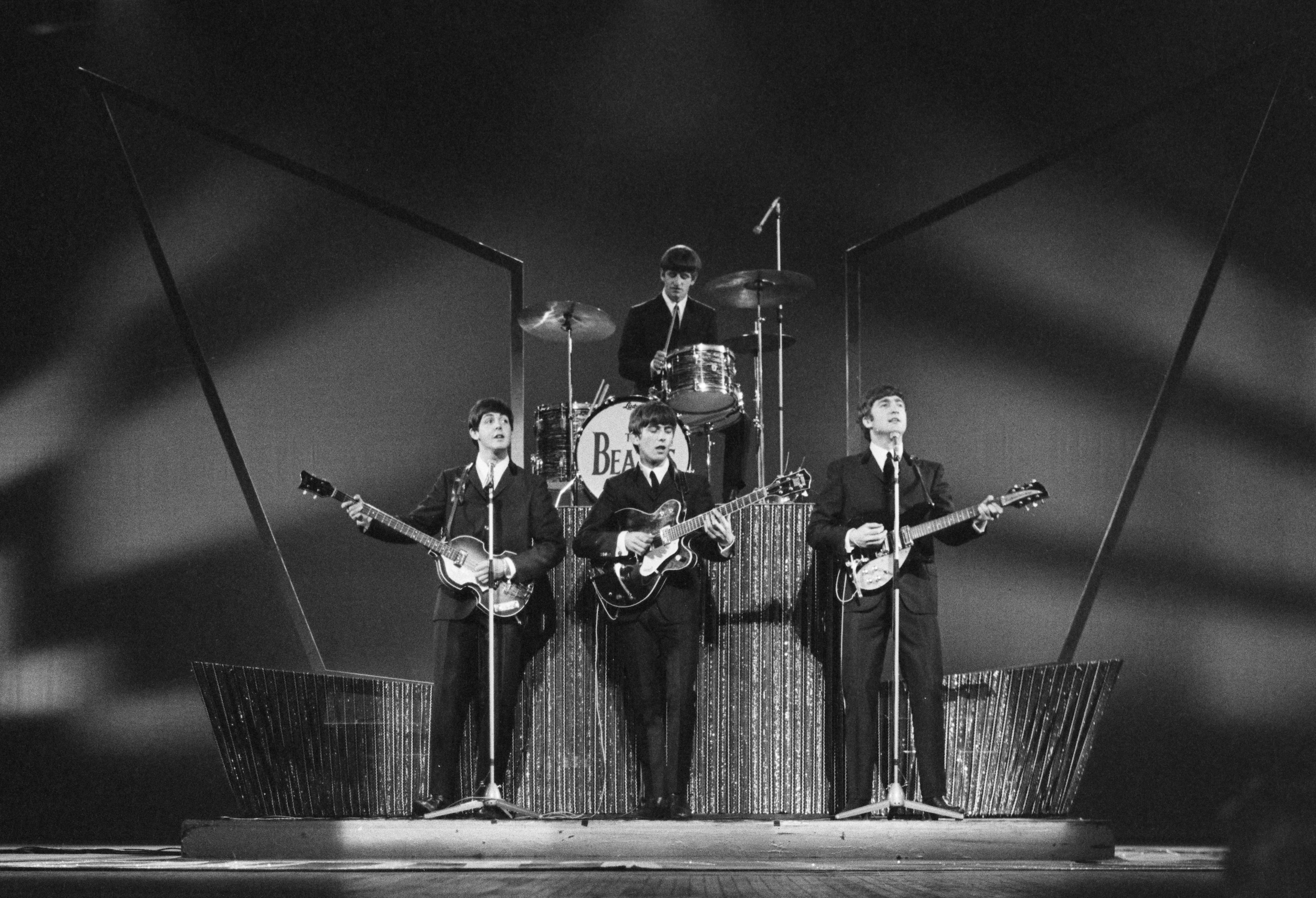The Beatles band performing on stage in black and white with guitars and drums