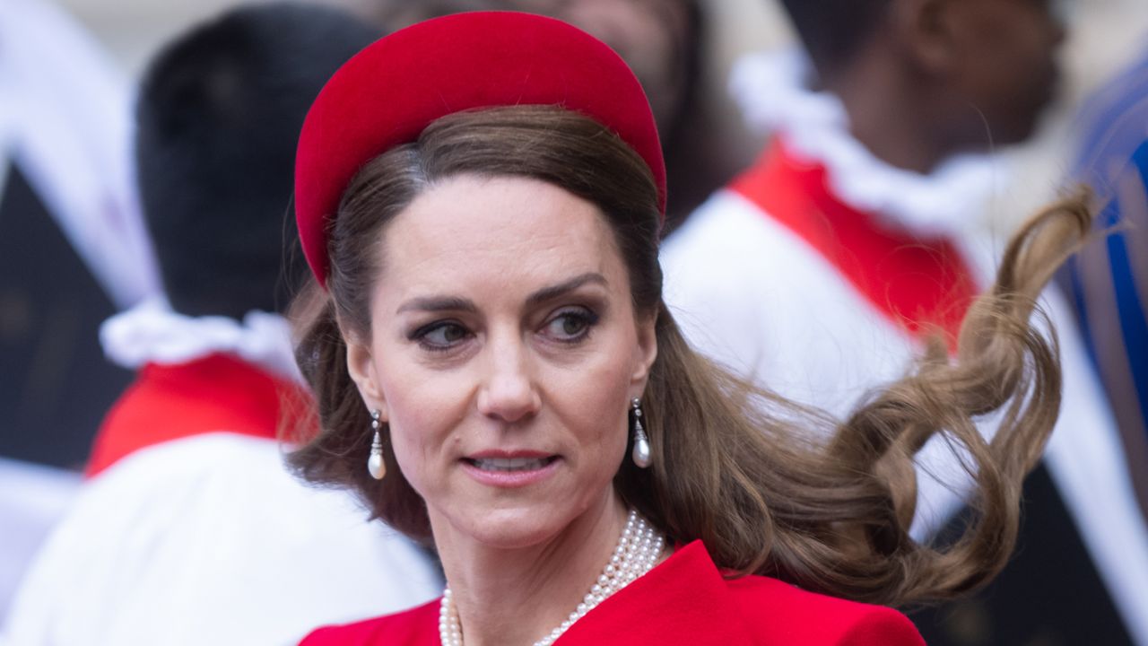 Kate Middleton wearing a red headband and coat with her hair blowing in the breeze on Commonwealth Day 2025