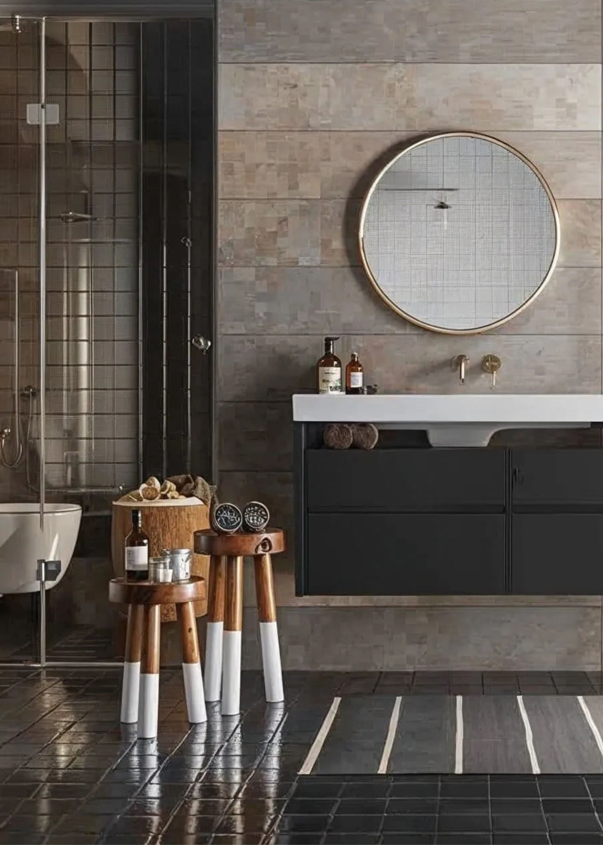 A bathroom with a dark vanity and a round mirror hanging above it as well as two small stools beside the vanity with bathroom essentials on top