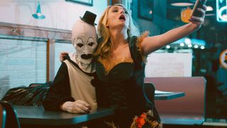 Art the Clown with a girl taking a selfie on his lap during the horror movie, Terrifier.