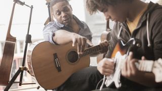 Man with acoustic guitar teaches another man with an electric guitar