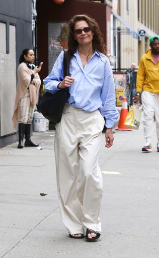 Katie Holmes styles cream wide leg trousers with a blue shirt.