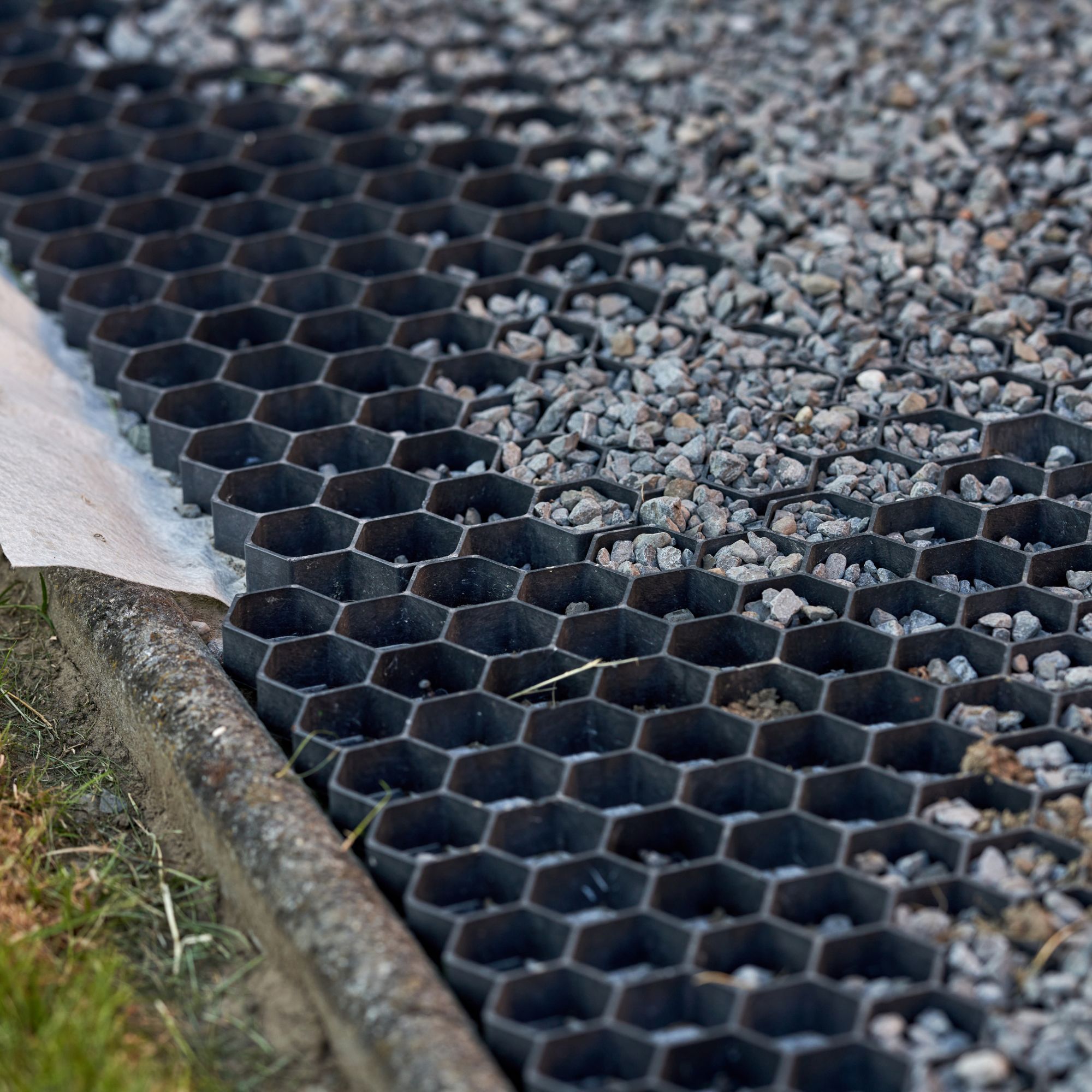 Close up of a gravel grid being laid and partially filled with gravel, with a weed membrane underneath