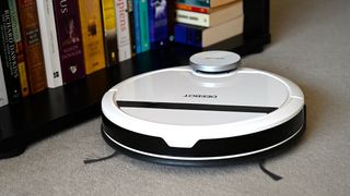 An Ecovacs Deebot 900 on a carpeted floor near a bookcase