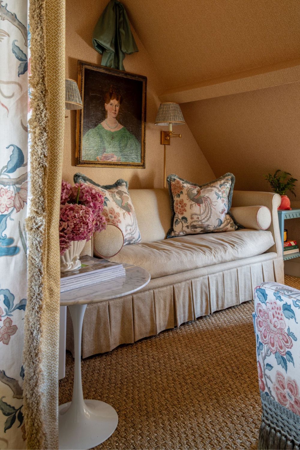 warm yellow wallpapered seating nook with a skirted couch styled with fringe trim patterned pillows sat opposite a floral arm chair with tassel trim