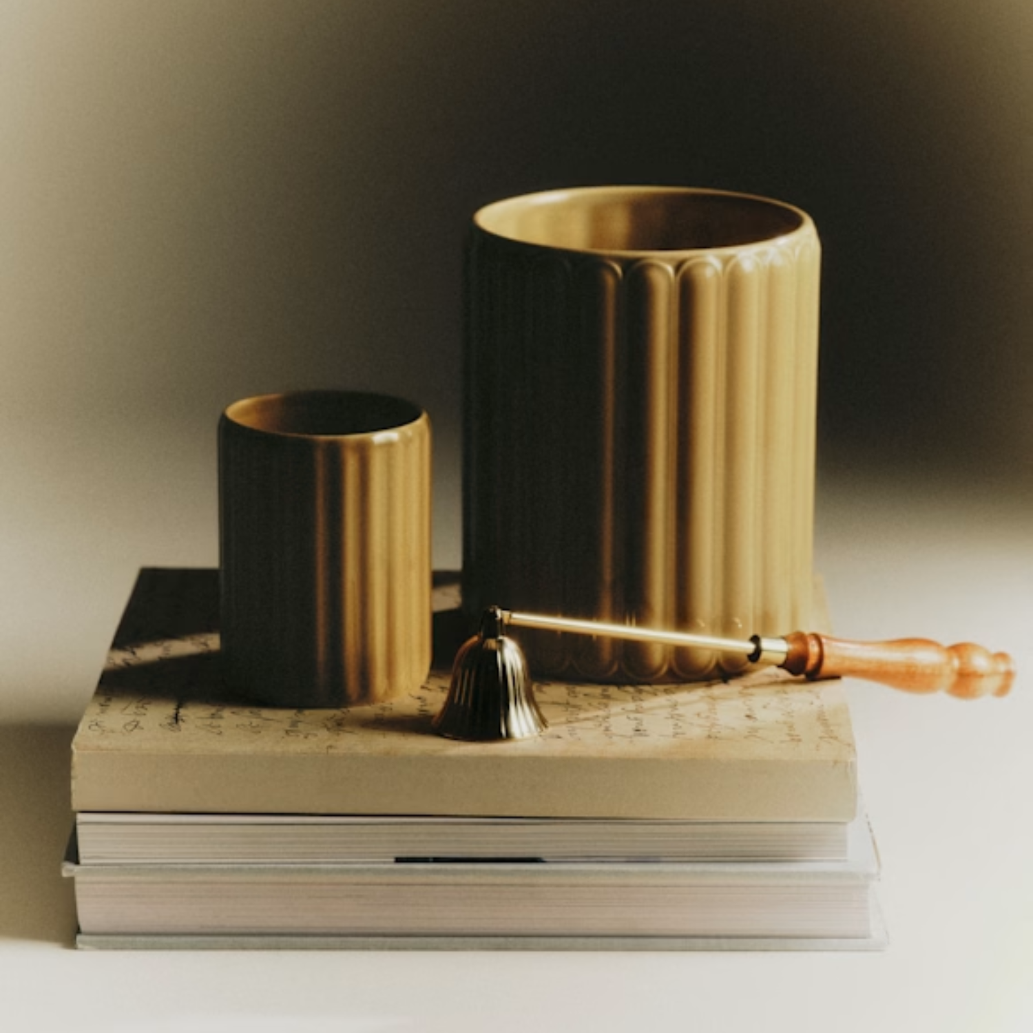 A ribbed green candle set on a stack of books by a candle snuffer