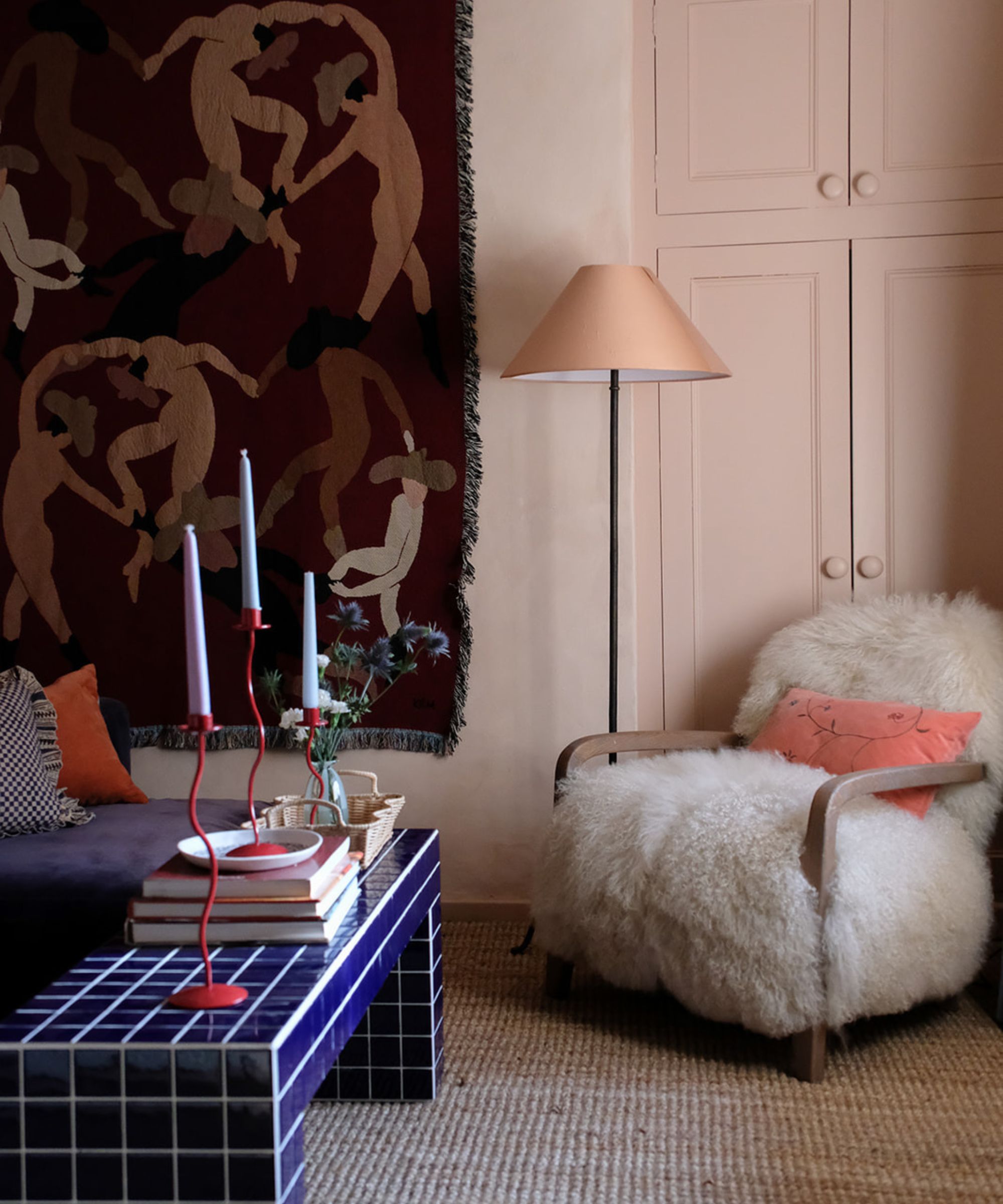 Eclectic living room with pink cupboard, fluffy armchair and blue tiled coffee table and tapestry hanging