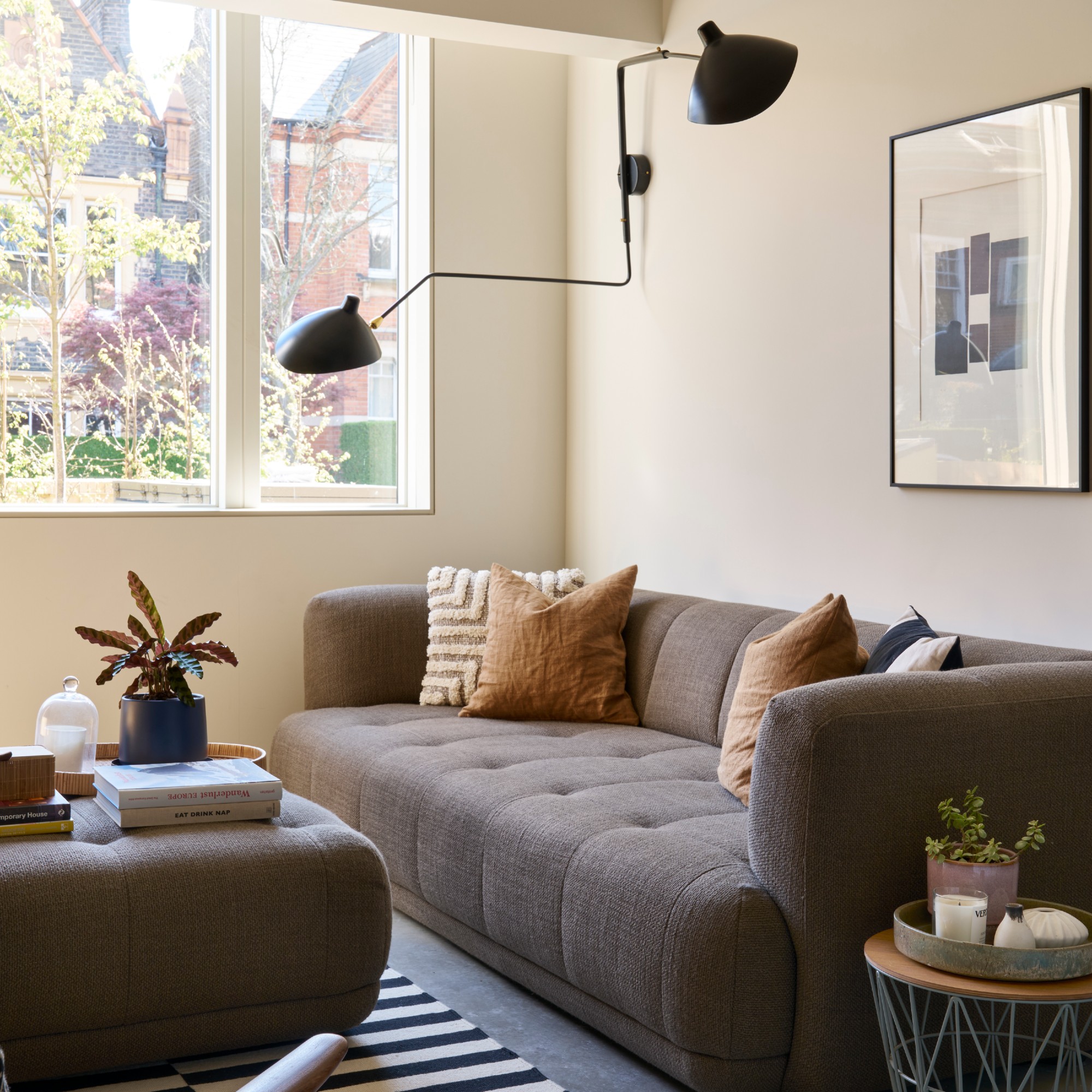 A warm cream-painted living room with a brown 3-seater sofa and a matching ottoman used as a coffee table