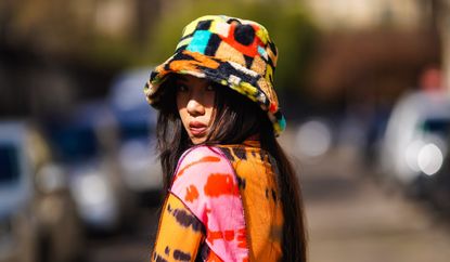 Alessandra Huynh @atiashuynh wears a fluffy colorful bob hat from Asos, a tie and dye multicolor top from Asos with printed patterns, a brown short vintage dress, on March 24, 2021 in Paris, France.