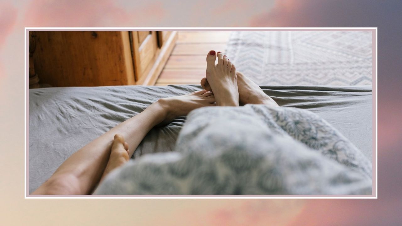 couples feet entangled at the end of the bed, against a pink background