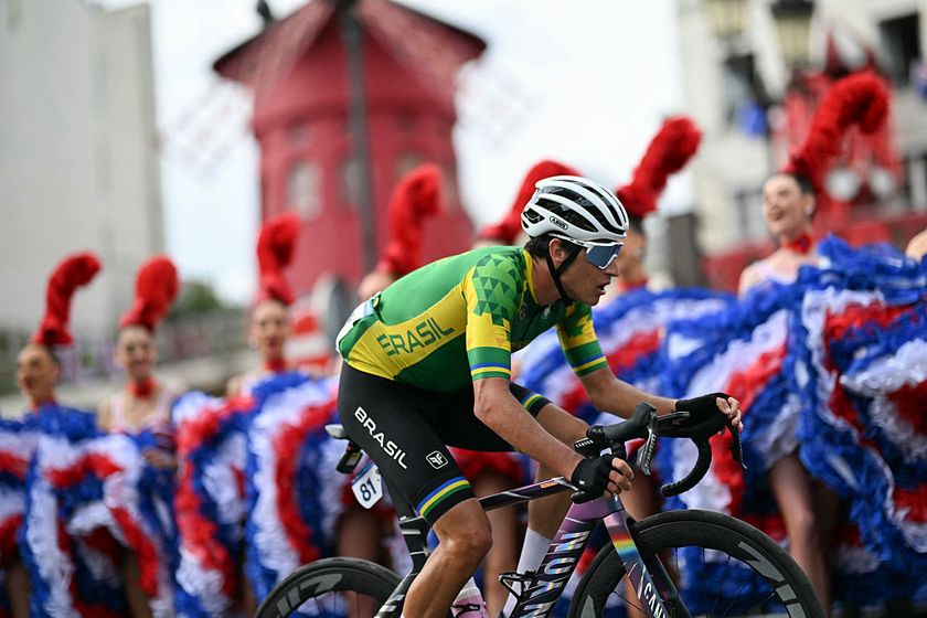 Brazil&#039;s Vinicius Rangel Costa cycles past Moulin Rouge dancers performing the cancan outside the Moulin Rouge cabaret during the men&#039;s cycling road race during the Paris 2024 Olympic Games in Paris, on August 3, 2024. (Photo by Mauro PIMENTEL / AFP)