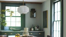 Anthropologie Eloise pendant light hanging in a verdant green kitchen with a wooden dining set