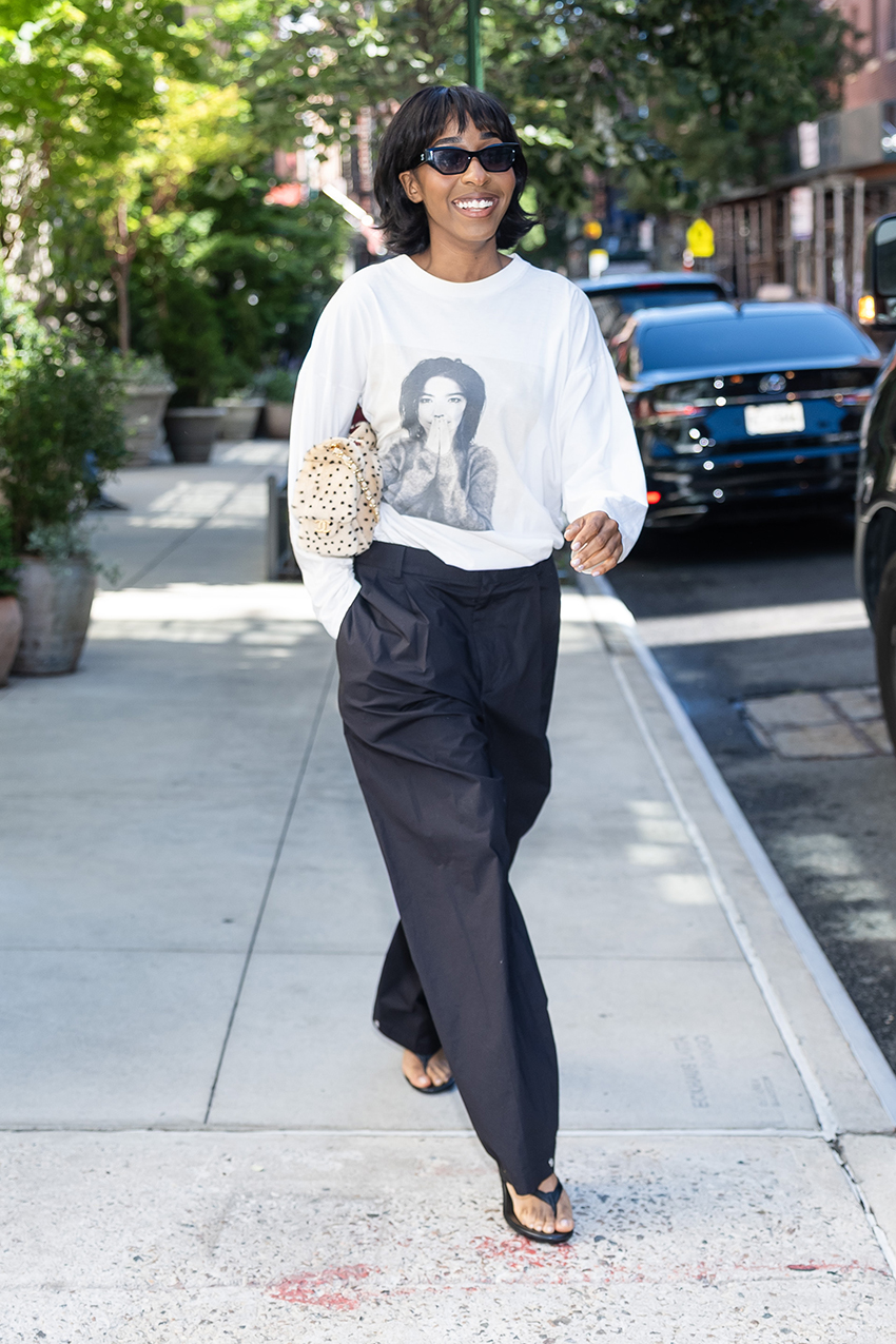 Ayo Edebiri wearing a white longsleeve Bkork graphic T-shirt, black tailored pants, and black thong sandals
