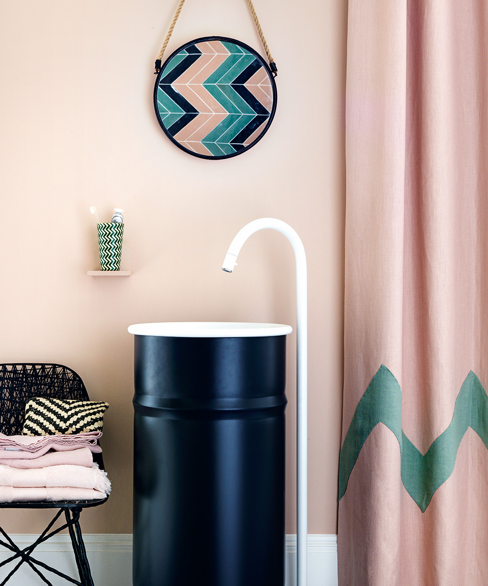 A pale pink bathroom with an unusual black sink with a white faucet