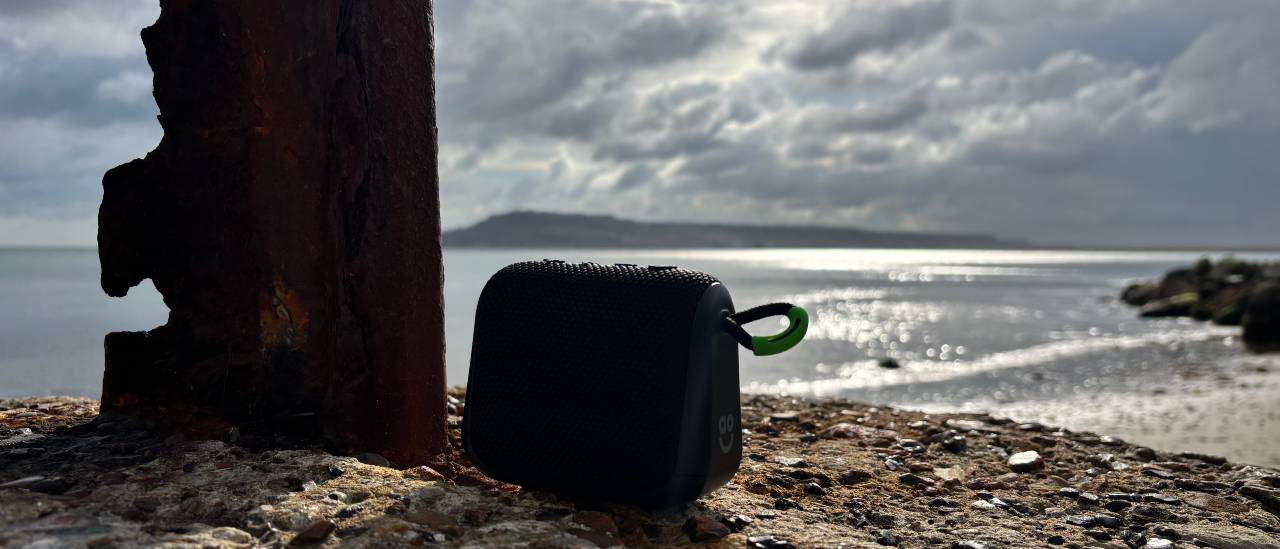 Black AO mini portable Bluetooth speaker on a rock with a habor and island in the background