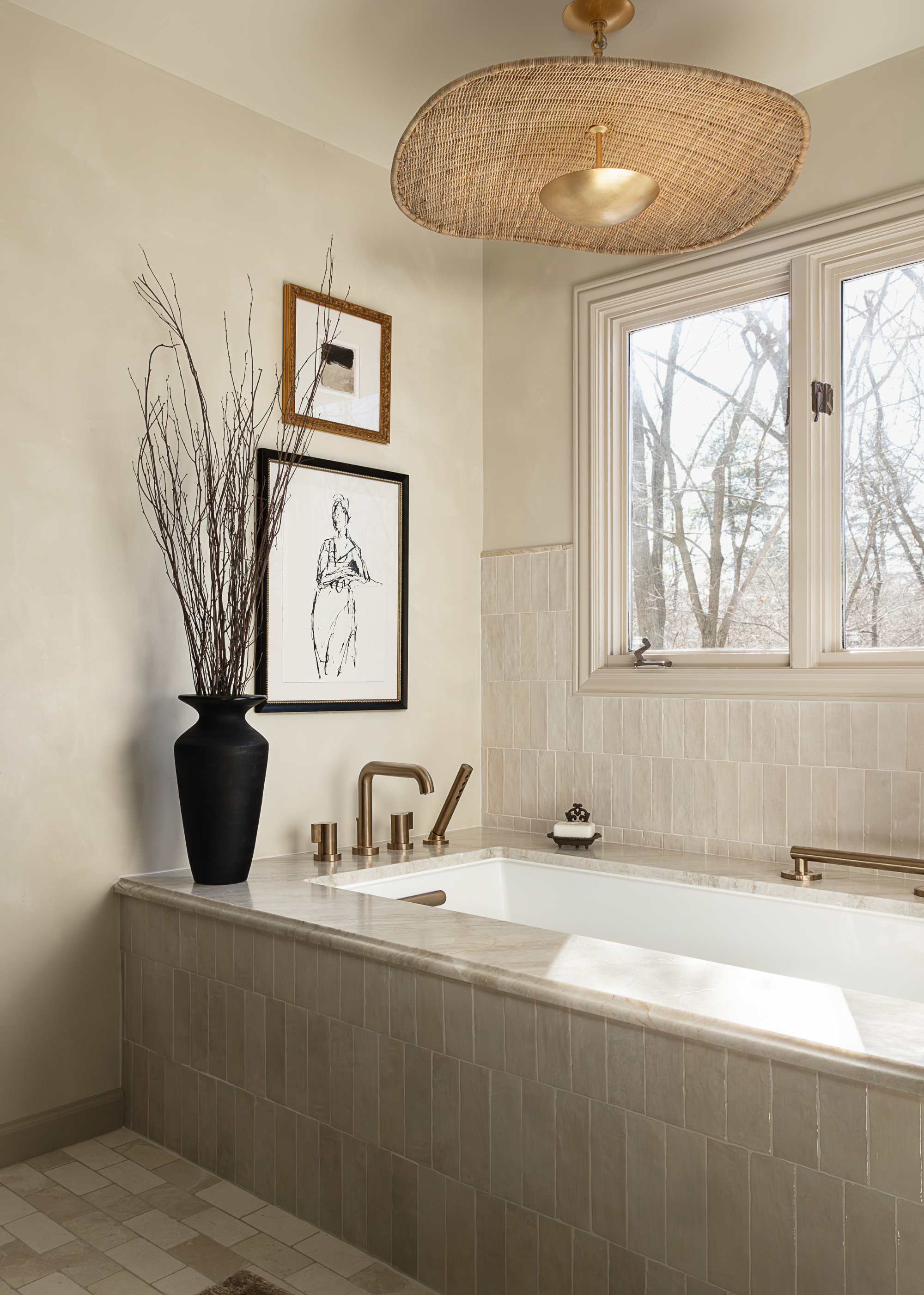 a built-in tiled bath with bronze fittings, a tall black vase on one edge, and a rattan and gold light fitting directly above the bath