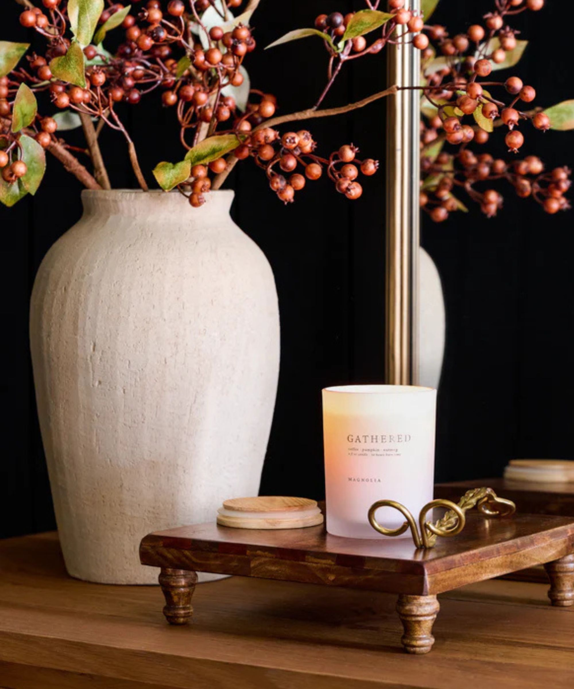 White 'Gathered' candle on a wooden tray next to a gold candle snuffer and a white stone vase