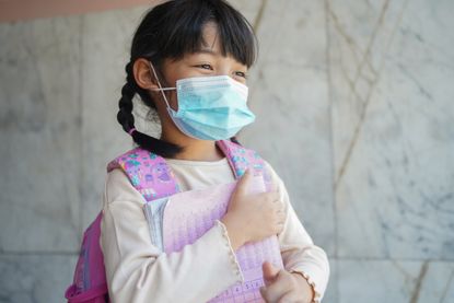 Young child with face mask on walking with books after getting Covid vaccine