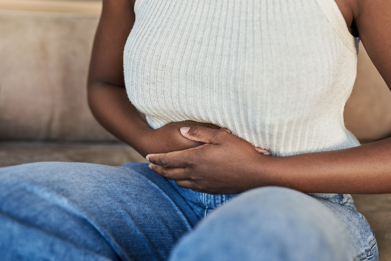 Cropped shot of a woman suffering from stomach pain on the sofa at home