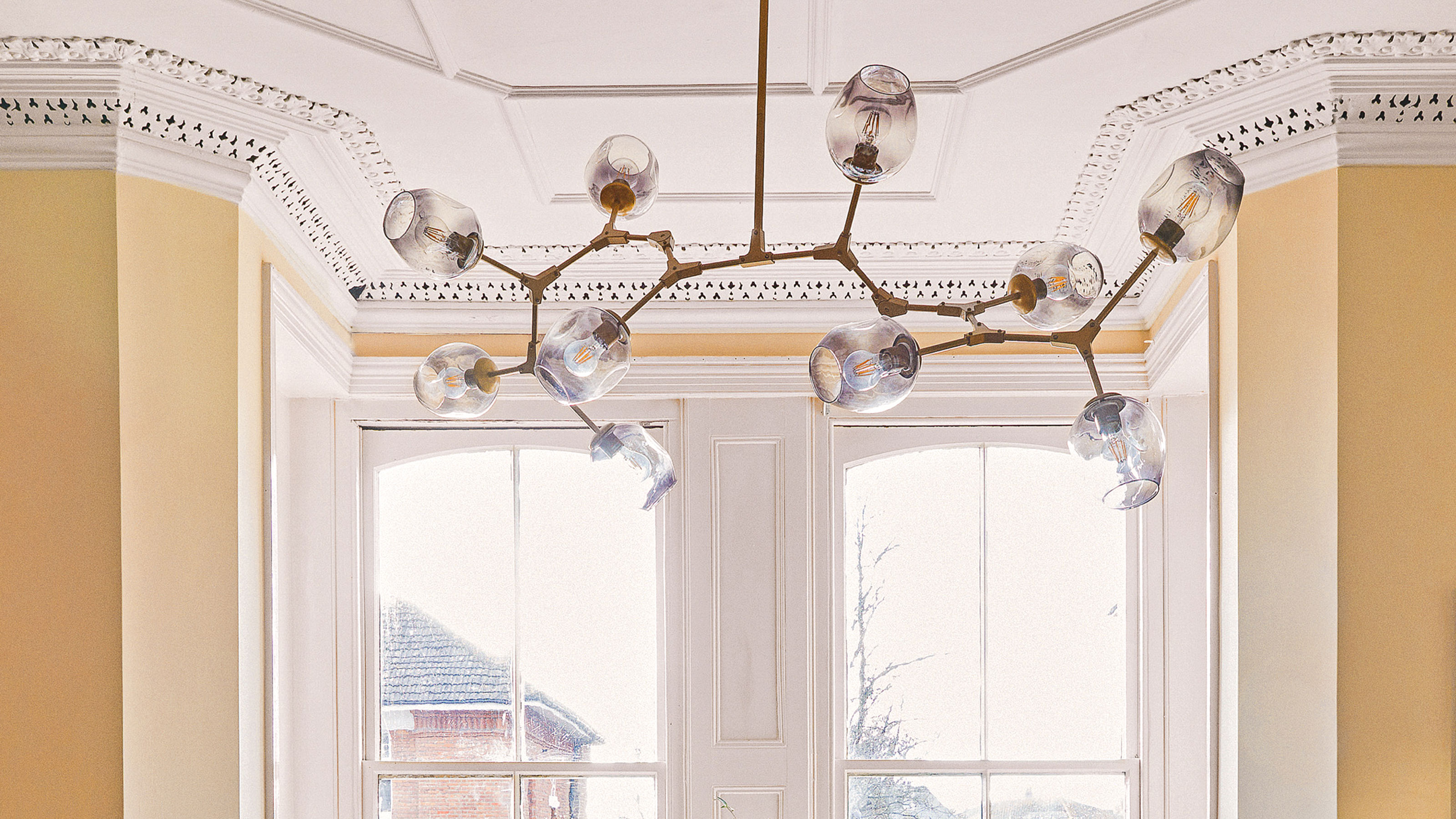 Glass and brass sputnik style light near bay window in yellow room