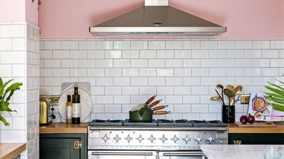 Open plan kitchen with pink walls, black Shaker style kitchen units, and rustic vintage furniture with stainless steel range cooker