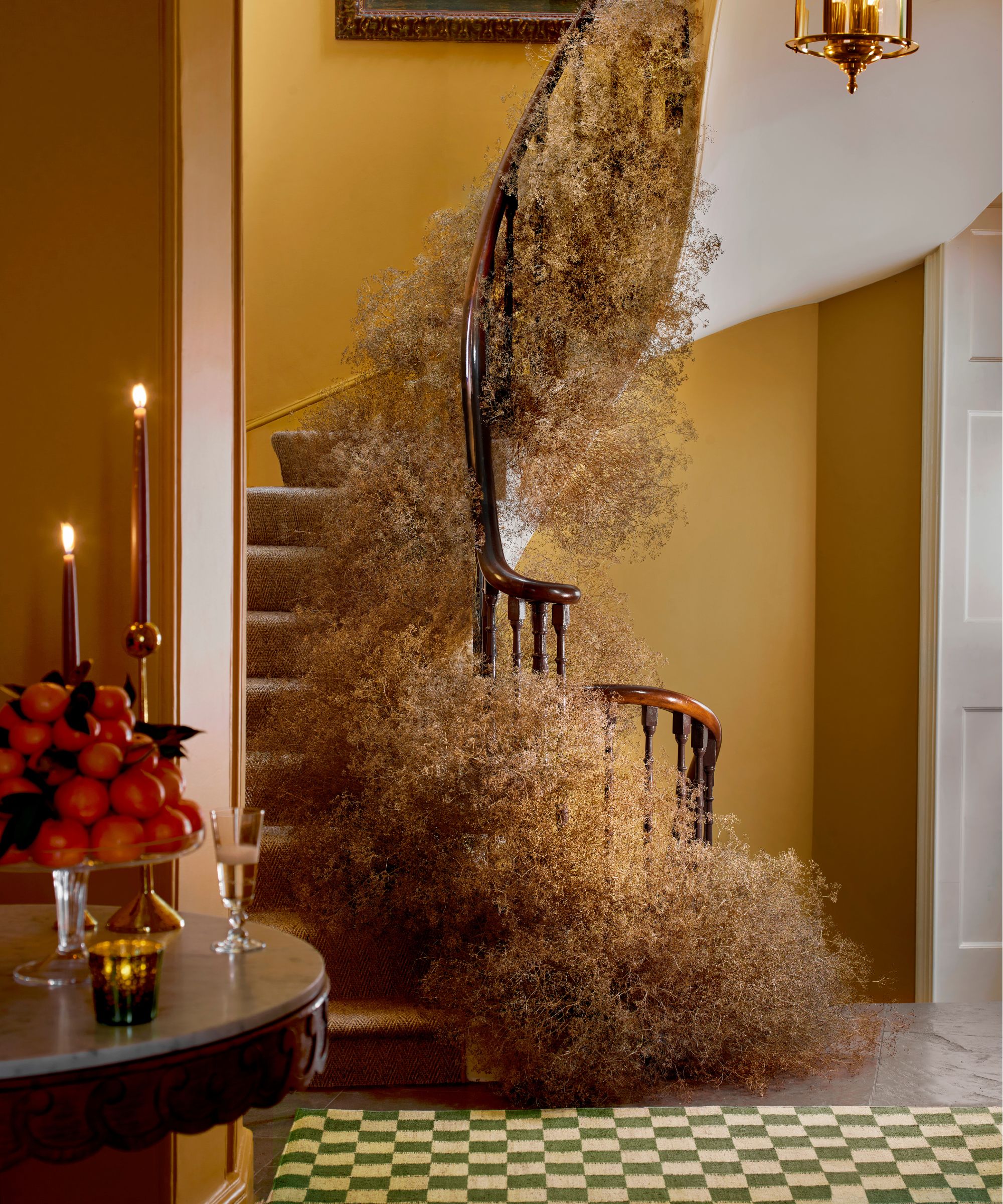 a large ochre painted hallway with winding staircase decorated with neutral foliage for the holidays