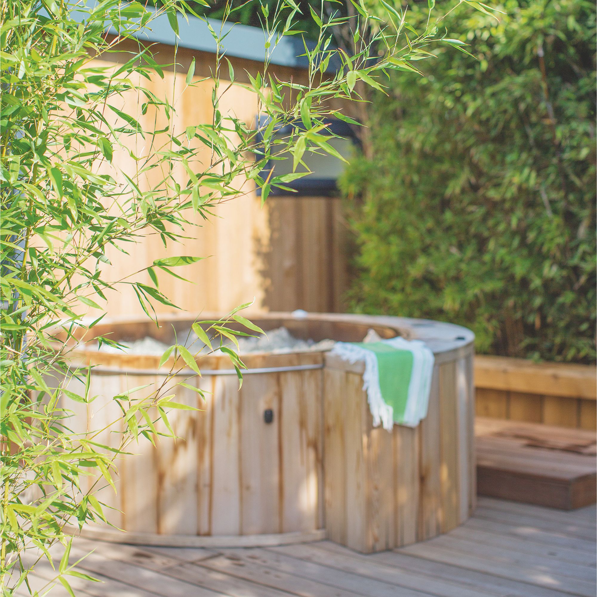 garden decking area with a wooden hot tub framed by green bushes