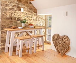 white and wooden breakfast bar table with stools against stone wall