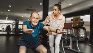 Man squats while personal trainer corrects his form