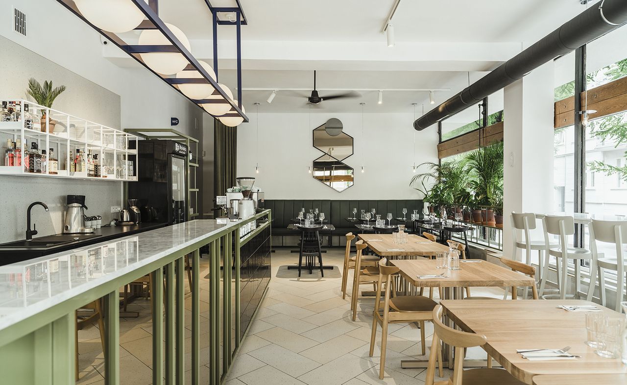 A long counter fronted with mirrors sits opposite a line of natural wood tables and chairs