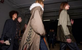 One model wearing a black coat with bag, one in a brown coat with white fur hood and one wearing a brown two-tone jacket