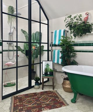 Bathroom with crittal style black framed shower, dark green freestanding bath, aztec rug and plants