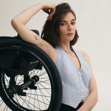 An Anthropologie model sits next to the wheel of her wheelchair posing with one arm up by her head while wearing a striped blue-and-white vest. 