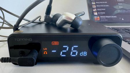 The Topping DX1 II DAC, with wired headphones resting on top, show the dB level on a white surface.