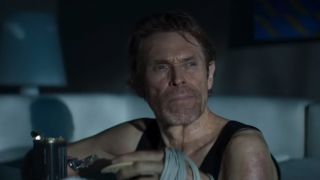 Willem Dafoe with a bandaged hand looking into the distance