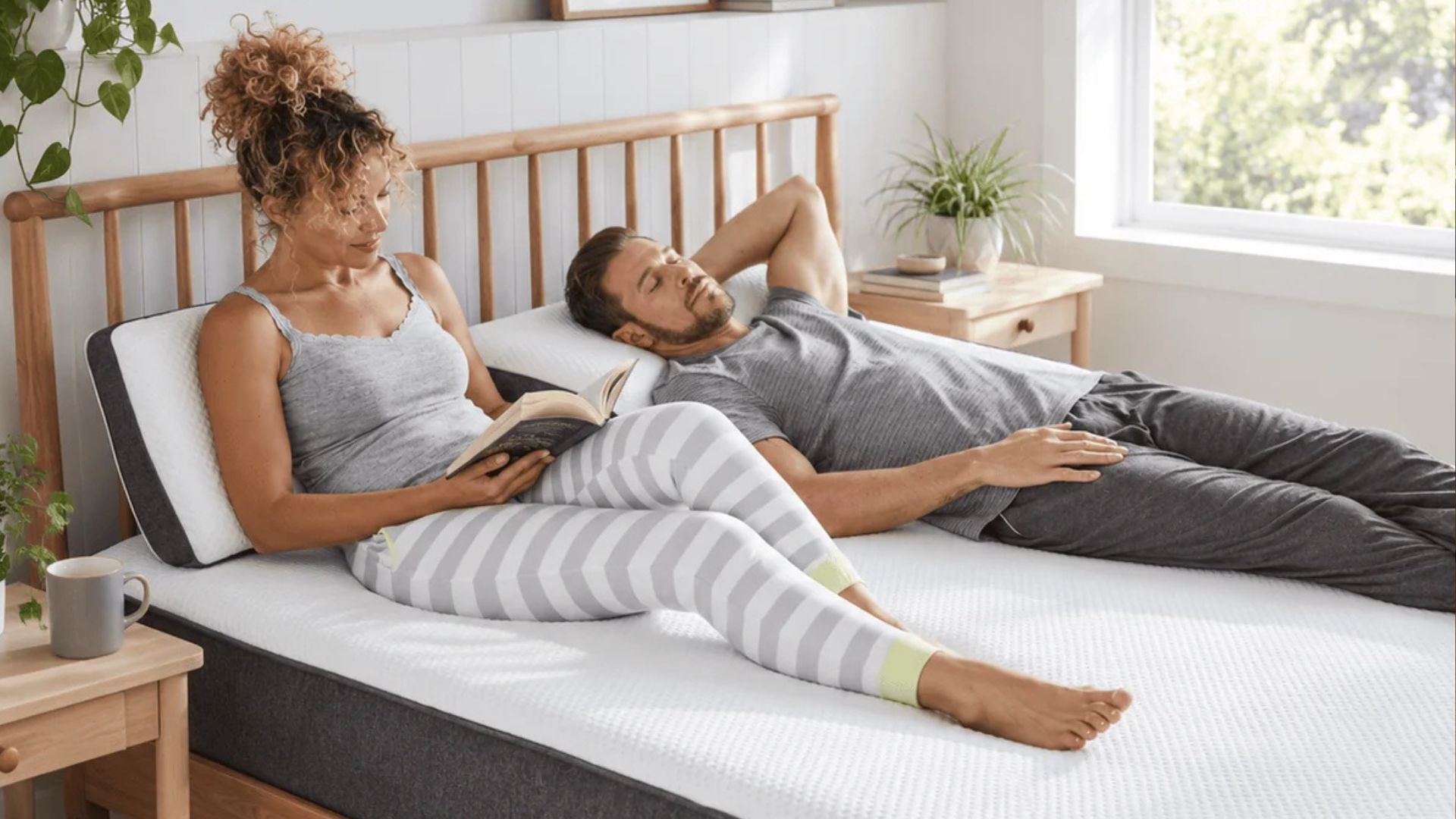 The image shows a young couple lying on the white and grey OTTY Original Ice Hybrid mattress, set within a neutrally decorated bedroom