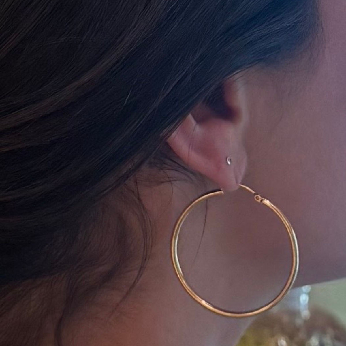 a close-up image of a girl with brown hair pulled back and a gold hoop earring with a stretched out piercing hole