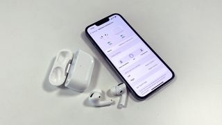 AirPods Pro on a table next to an iPhone showing the settings screen