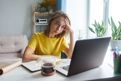 A woman in a yellow shirt looks forlornly in front of a laptop